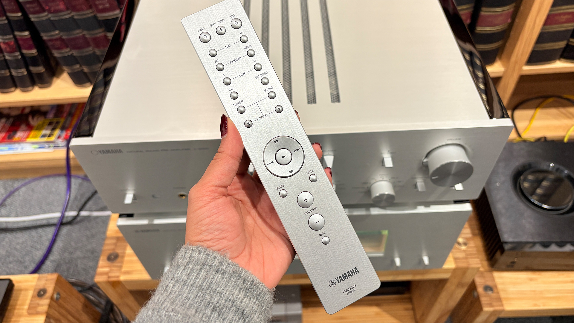 Hand holding silver remote control in front of Yamaha C-5000/M-5000 pre/power amplifier