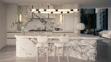 Image of an all white, ultra modern kitchen with a curved kitchen island made out of white marble. The backsplash and hood are in a matching marble and there is an abstract pendant light hanging over the island.