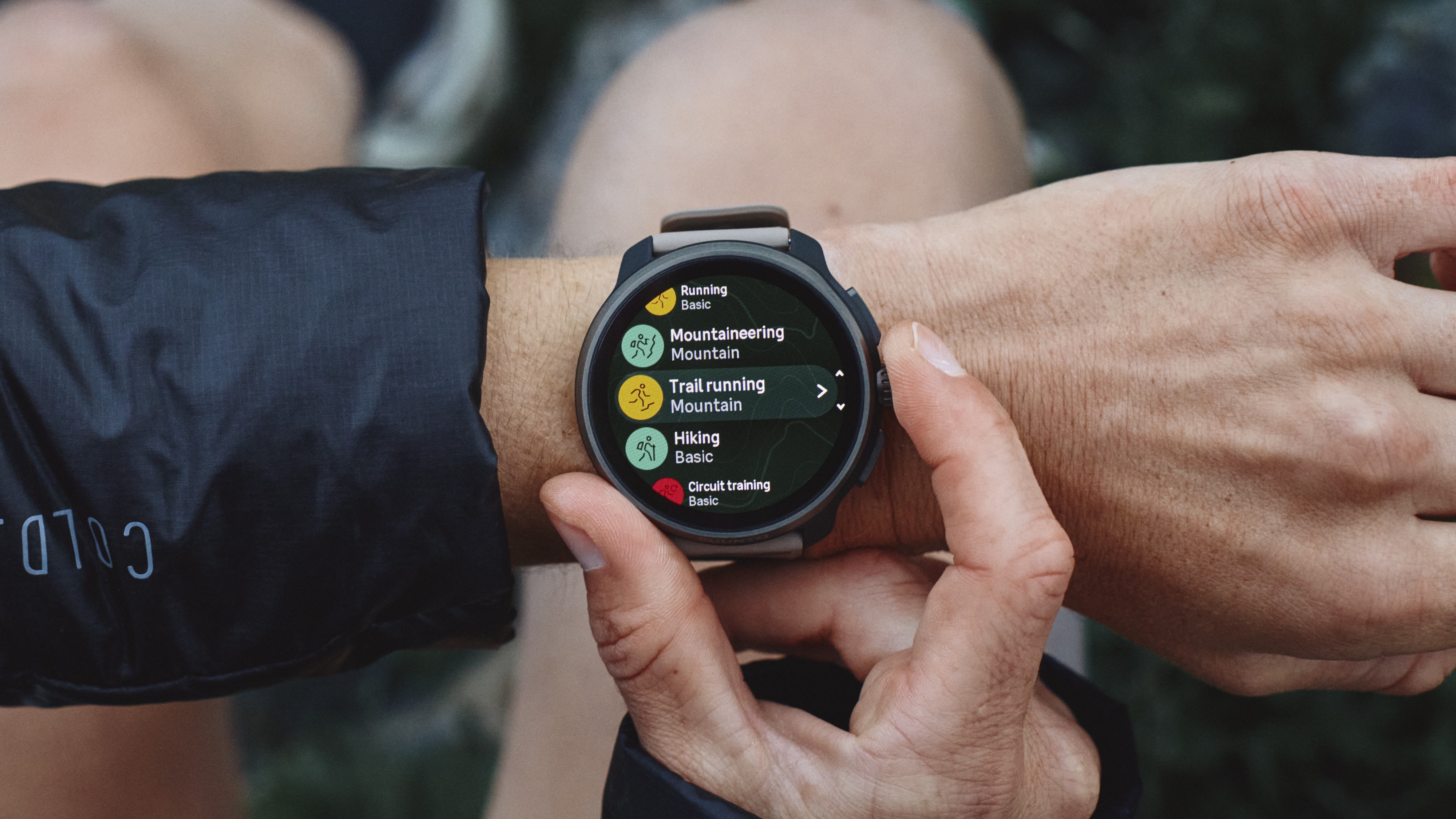 Photo of the Suunto Race 2 running watch on a person&#039;s wrist, their fingers primed to press a button to select a Trail Running activity on the watch.