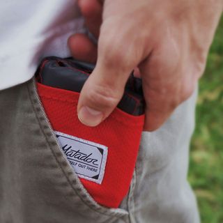 Man putting red folded Matador Pocket Blanker into his pants pocket