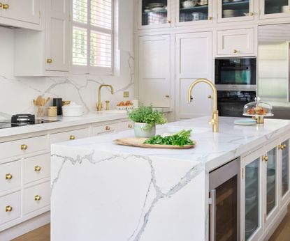An all white kitchen with marble countertops, floor-to-ceiling cabinets, and gold hardware