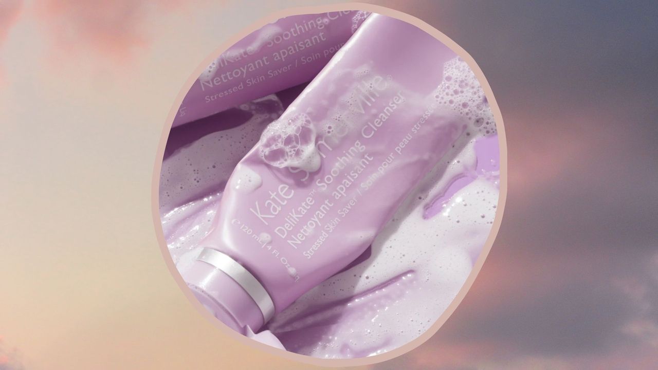 A pink and grey cloudy background with a circular image of kate somerville delikate cleanser lathered up with soap suds