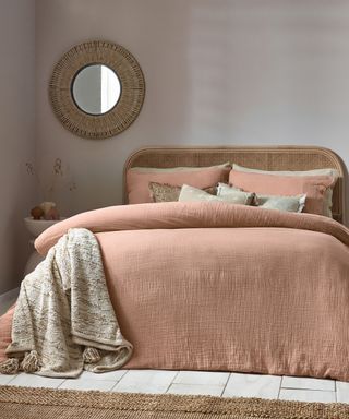 A gray bedroom with a brown bed with pink bedding and a gray blanket