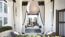 A sheltered outdoor area with a spherical lampshade, garden furniture, and curtains with black trim