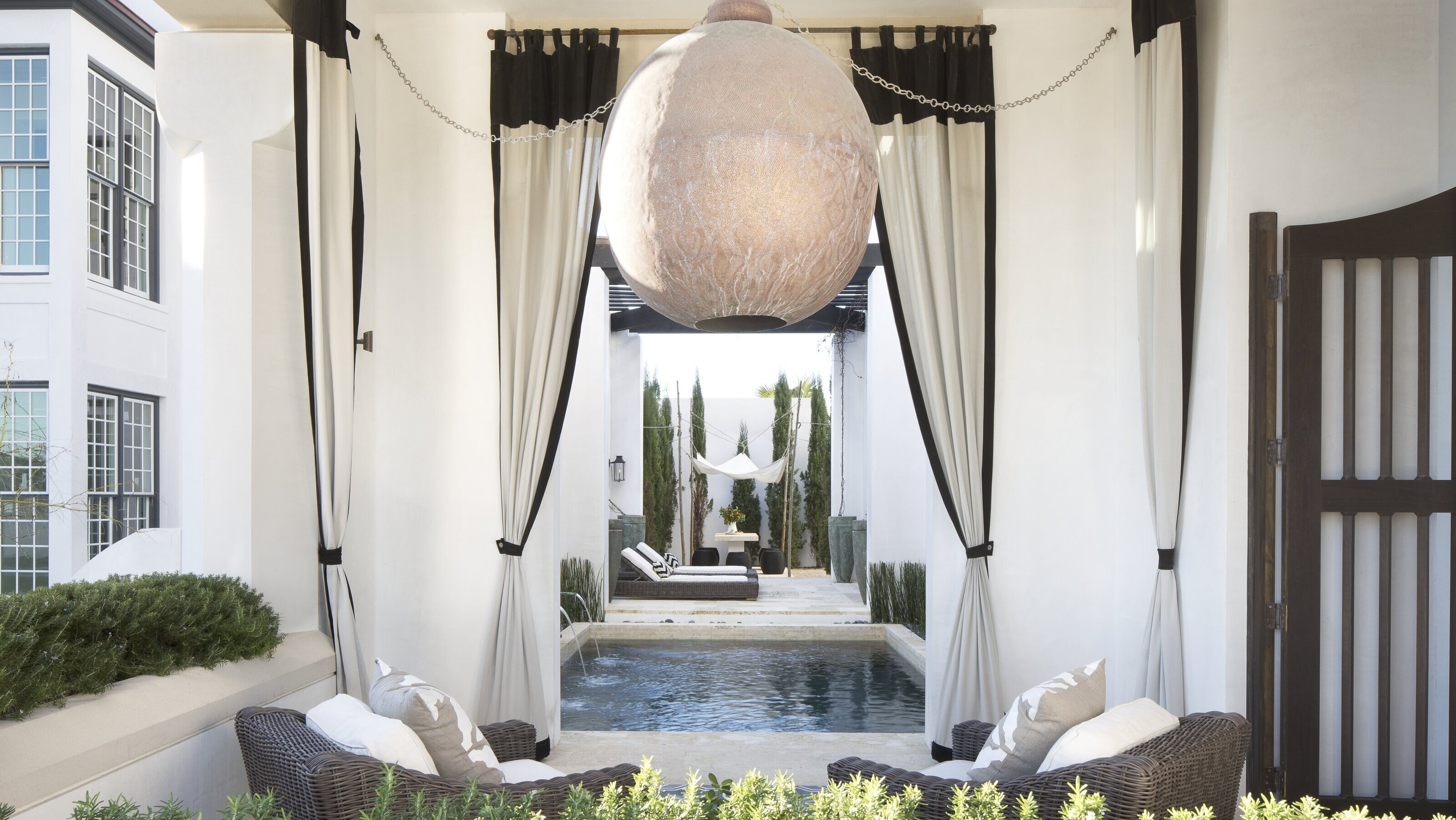 A sheltered outdoor area with a spherical lampshade, garden furniture, and curtains with black trim 