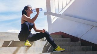 a woman wearing exercise wear sitting on a step drinking from a water bottle