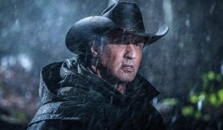 Rambo V: Last Blood John Rambo stands in the rain, with a black coat and cowboy hat