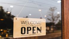 Welcome we are open sign hanging in shop window.