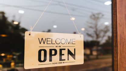 Welcome we are open sign hanging in shop window.