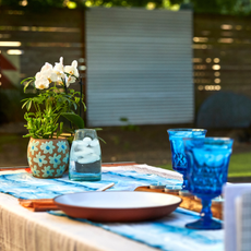 An outdoor table covered in tablescaping accessories, such as a blue table runner, blooms, and glassware
