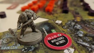 A miniature of a dwarf warrior stands on board tiles, looking off at tokens in the distance