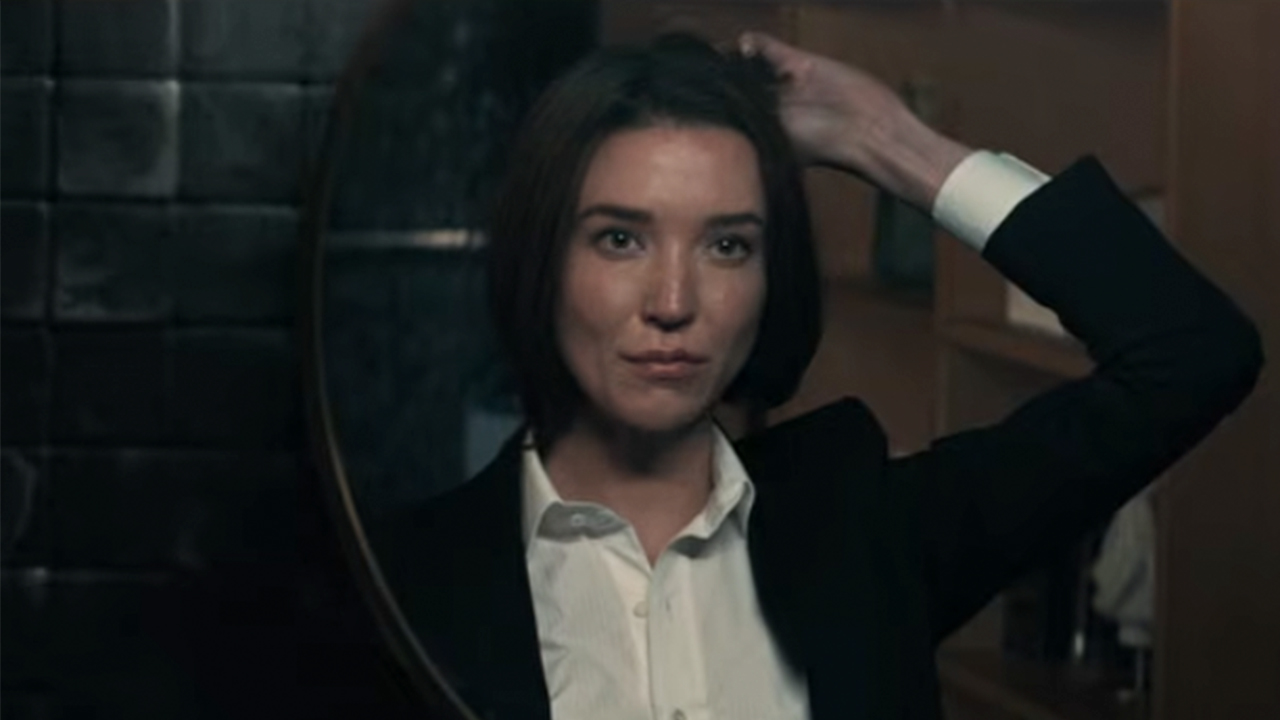 Nicole Brydon Bloom holding her hair up and looking in a mirror in Paradise