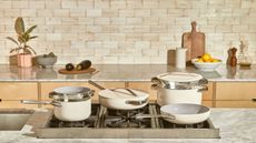 A cream ceramic Caraway cookware set on a gas stove in a modern kitchen