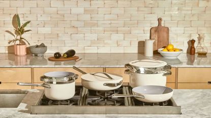 A cream ceramic Caraway cookware set on a gas stove in a modern kitchen