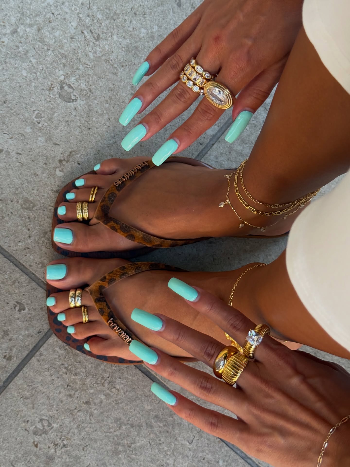 long square nails and matching toes painted a bright opaque teal, paired with stacked gold rings and anklets