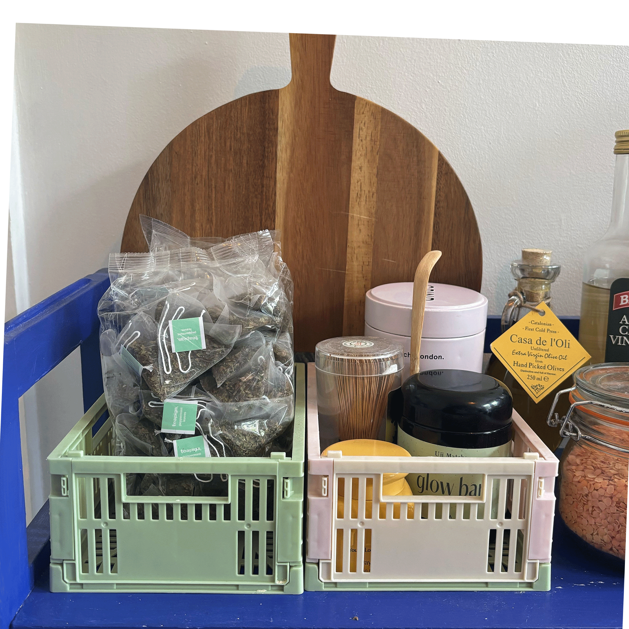 Colourful Primark storage crates in green and pink holding tea supplies on blue shelves