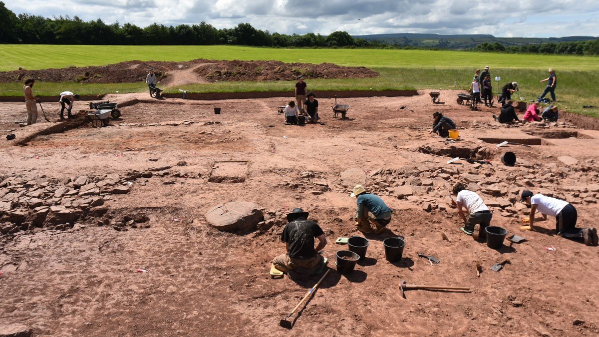 Close up of a Neolithic burial site at Dorstone Hill in the west of England. Here we see a large rectangle that has been dug up in a grassy field. There are a lot of people working on the site.