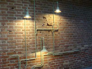 A network of pipes on a brick wall, illuminated by three lights