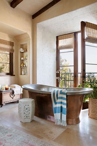 copper bath with open french window with pale stone floors
