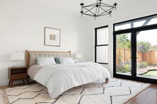 A bedroom with a cream-toned carpet, white bedding, white walls and a chandelier on top