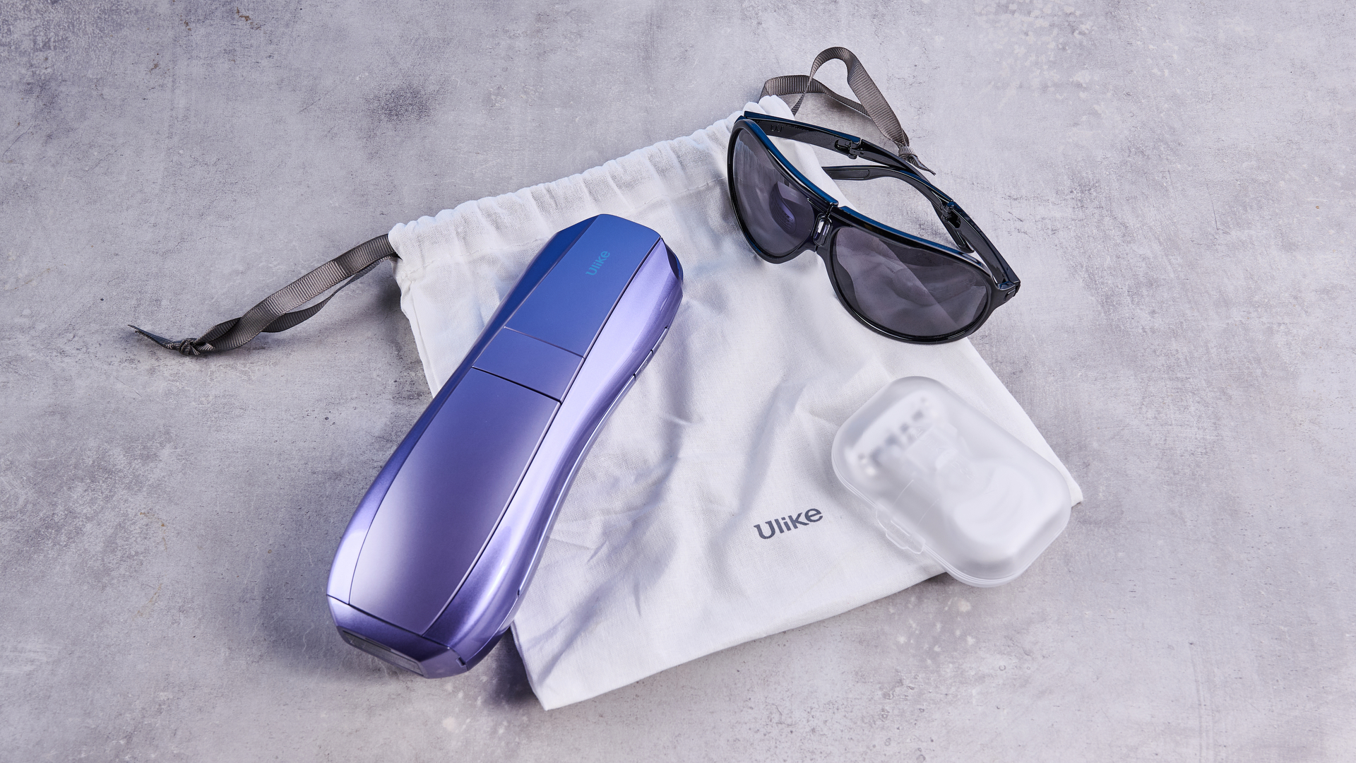ULike Air 10 IPL machine with fabric pouch, goggles and razor, photographed in front of a gray background.