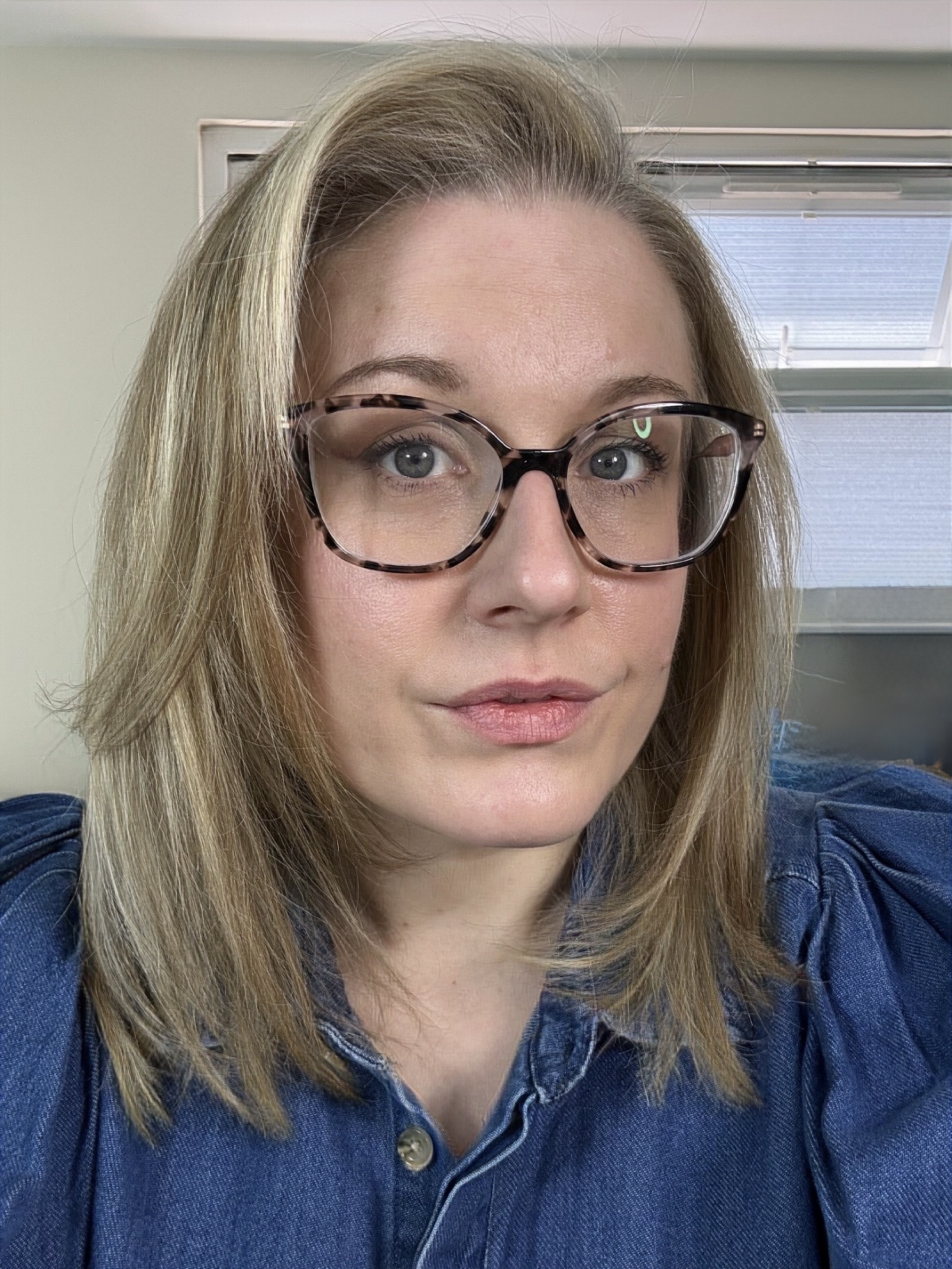 A woman with shoulder-length blonde hair and glasses looking at the camera, her hair styled with visible volume and smoothness