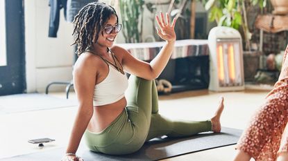 A woman performs a seated twist on a yoga mat. She is sat with her left leg extended on the floor and her right leg cross over. She twists to the side and her left elbow rests on her right knee.