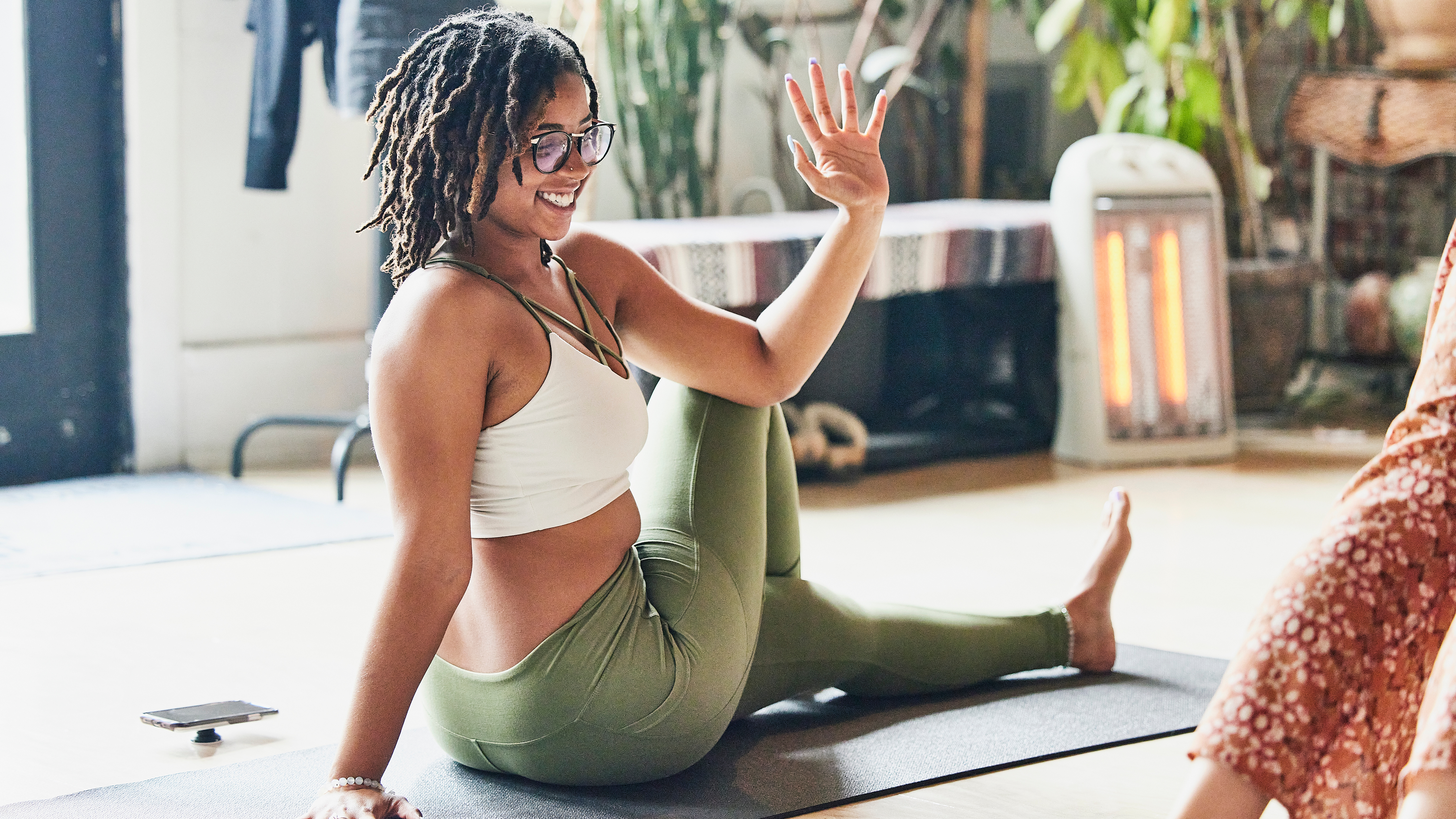 A woman performs a seated twist on a yoga mat. She is sat with her left leg extended on the floor and her right leg cross over. She twists to the side and her left elbow rests on her right knee.