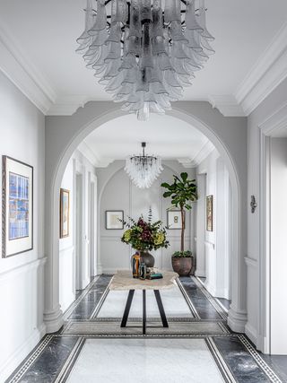 hall with grand arches and white walls with rough hewn slab table and big flower arrangement and modern artworks and chandeliers