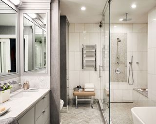 Large modern bathroom gray herringbone floor tiles, large cream wall tiles, large walk in shower section, leather seat with metal frame, sectioned sink and toilet space