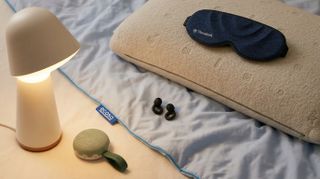 A smart lamp, quilt, white noise machine, pillow and eye mask on the floor