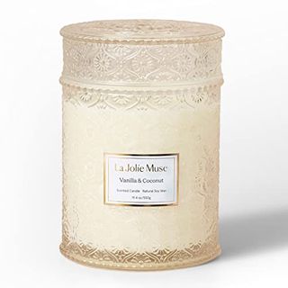 Cream candle in patterned like lace glass jar. It has a white rectangular classic looking label with gold embossing featured around the edge and on brand name