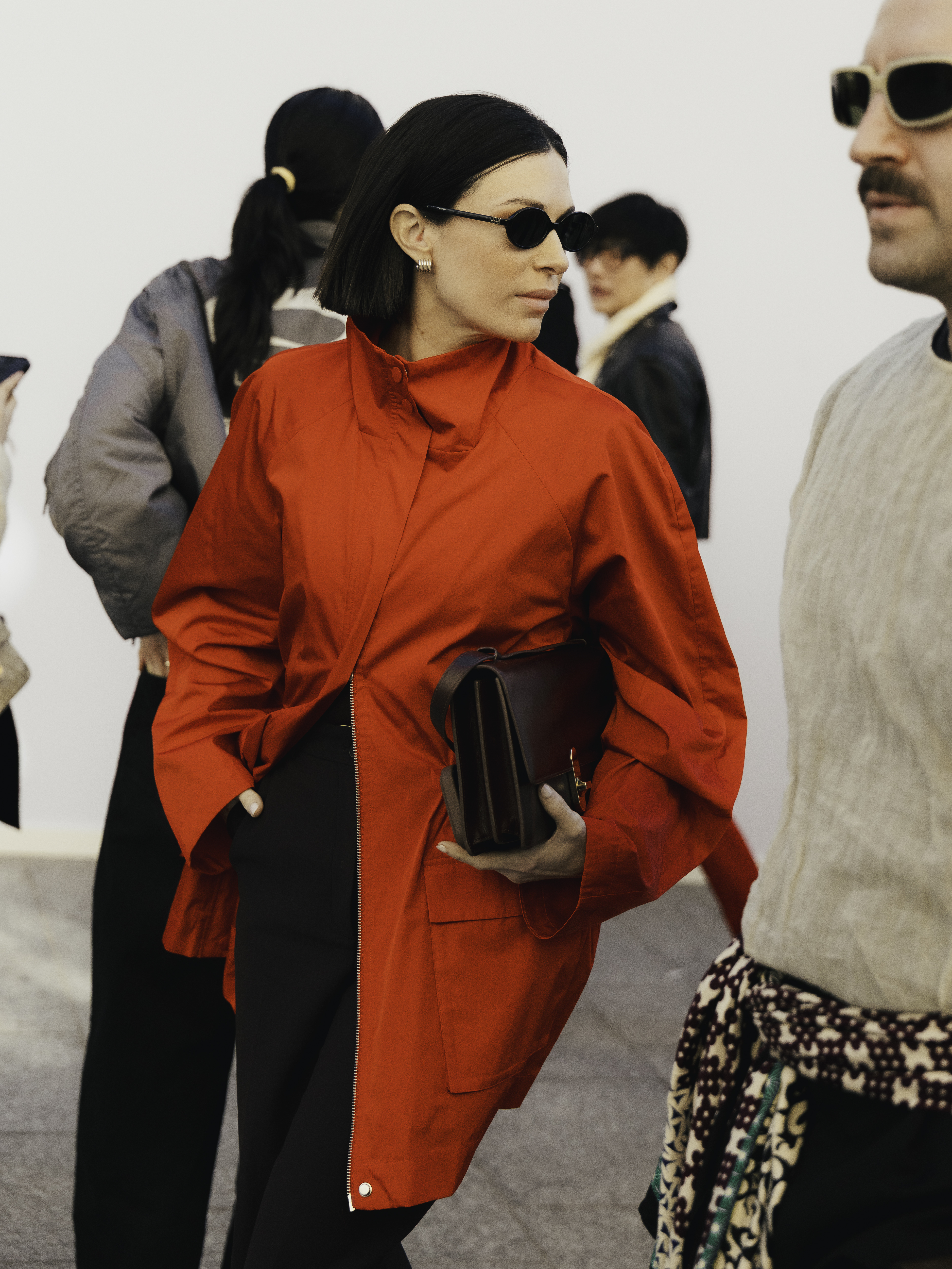 woman wearing red jacket, black pants, and black clutch
