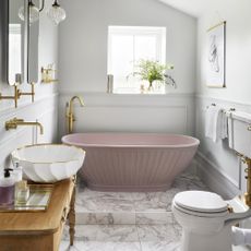 Bathroom with pink freestanding bath and gold fittings.