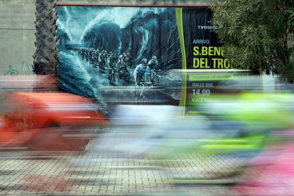 The peloton speeds past a race poster