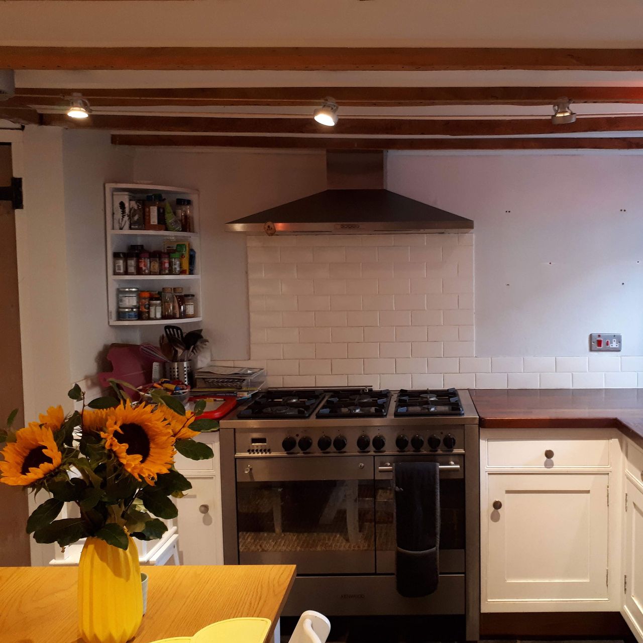 Kitchen with wooden ceiling beams, range cooker and wooden table with vase of sunflowers