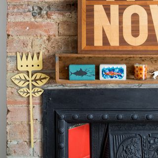 A black fireplace with fish-print matchboxes on the mantelpiece and a slogan artwork hung above it