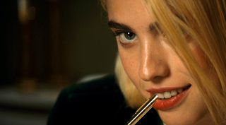Neon Films Margaret Qualley as Rebecca, biting a pen, in Sanctuary