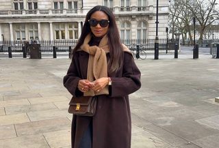 Woman wearing a brown wool coat with a tan sweater tied around her shoulders.