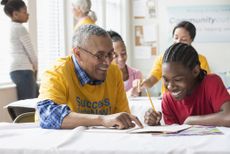 A retiree volunteers by tutoring a student in the classroom.