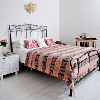 white walled bedroom with floorboards and iron bed