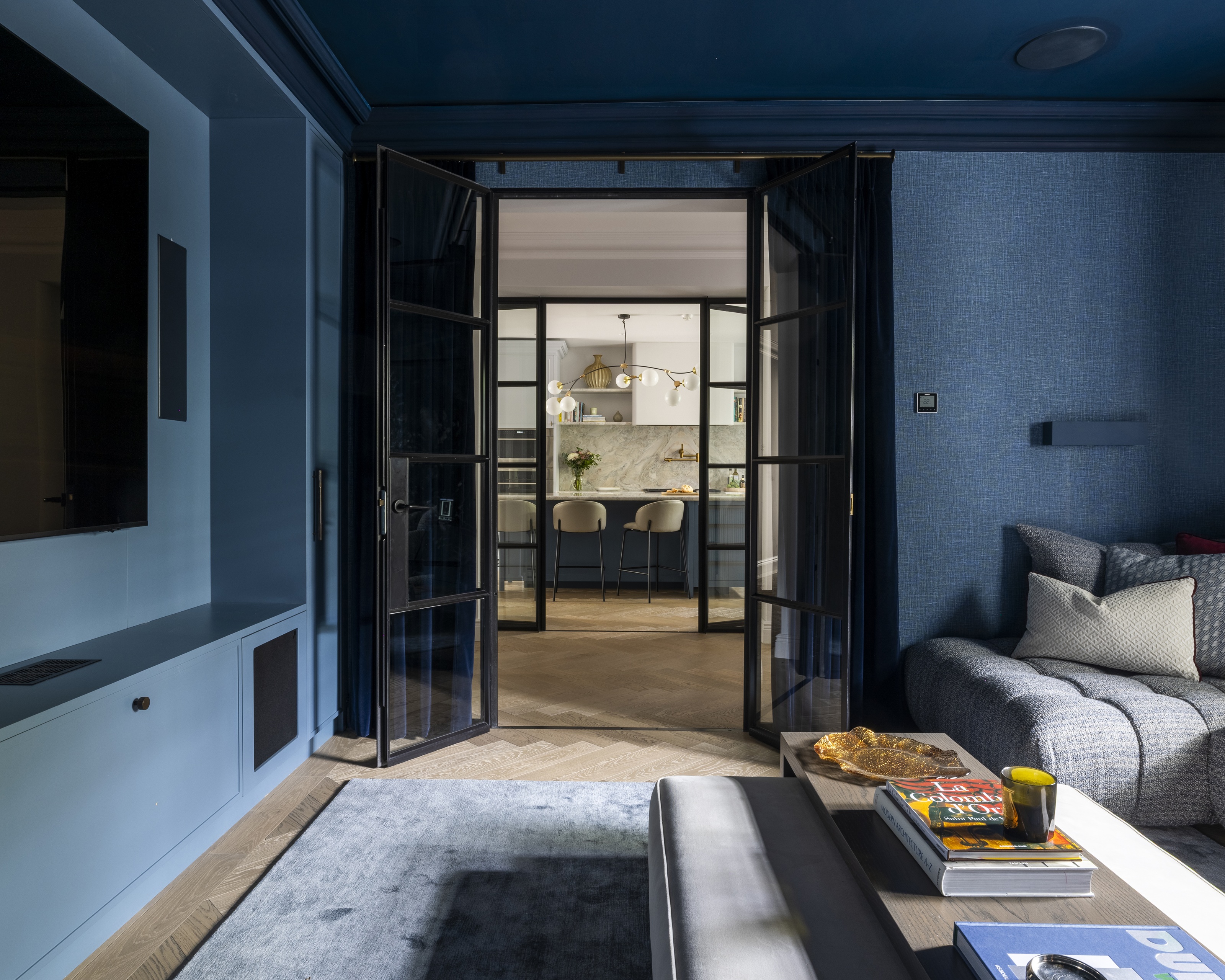 a dark blue cinema room with a curtained door and a comfy grey sofa