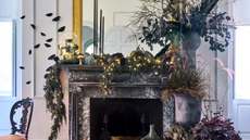 a fireplace that's been elaborately decorated for halloween with garland, potted plants, wall-mounted moths, and decor in dark colors