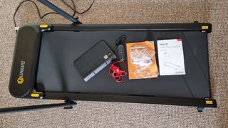 Urevo Strol 2E treadmill with a device mount, instructions manual, remote control, magnetic safety clip and other tools provided in the package