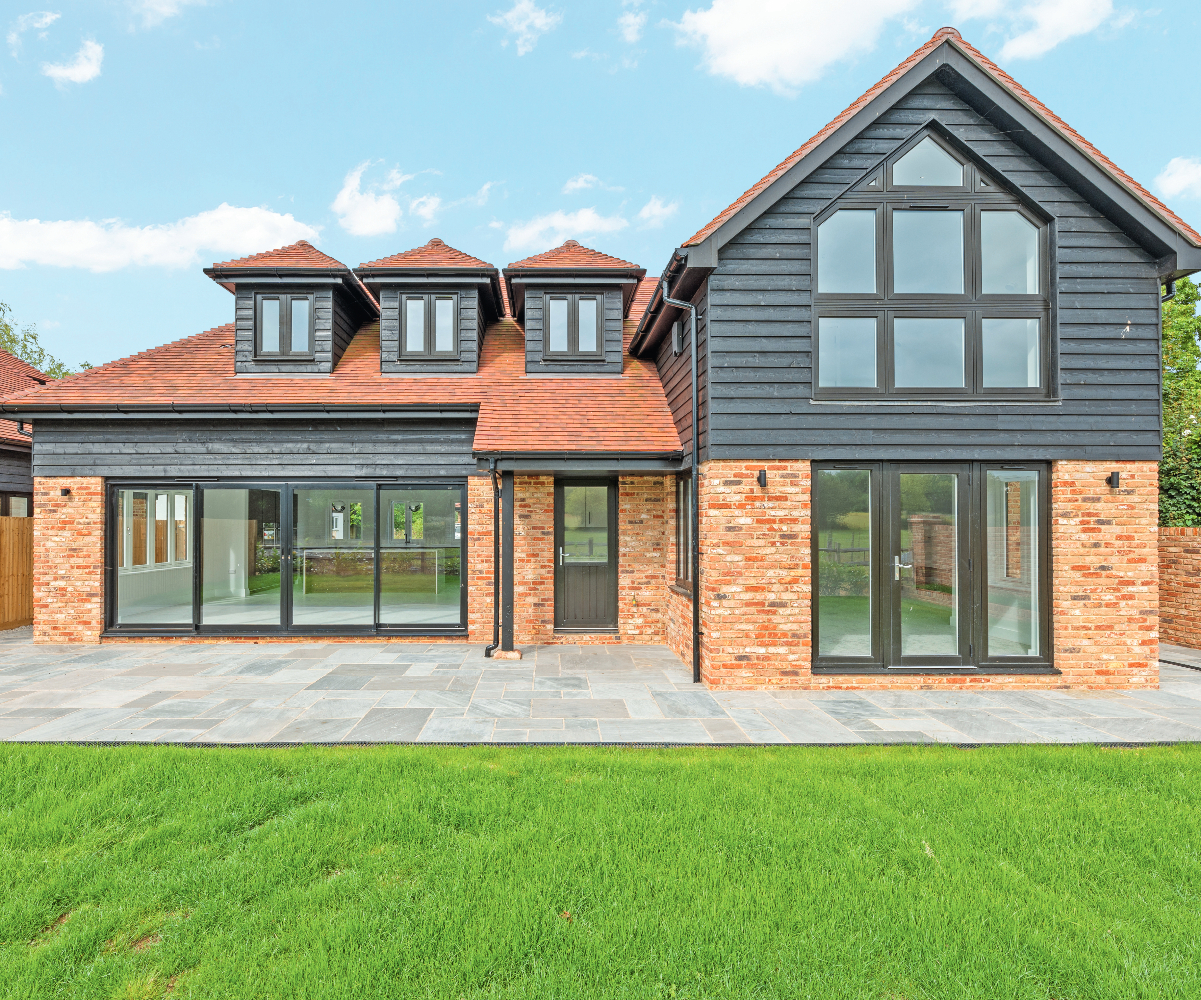 modern self build with brick and dark wood cladding, large bifold doors and dormer windows in roof