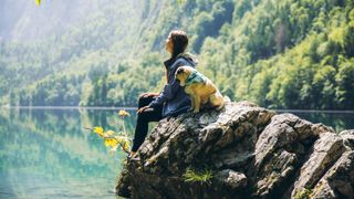 Woman sat with her dog on a rock overlooking a lake