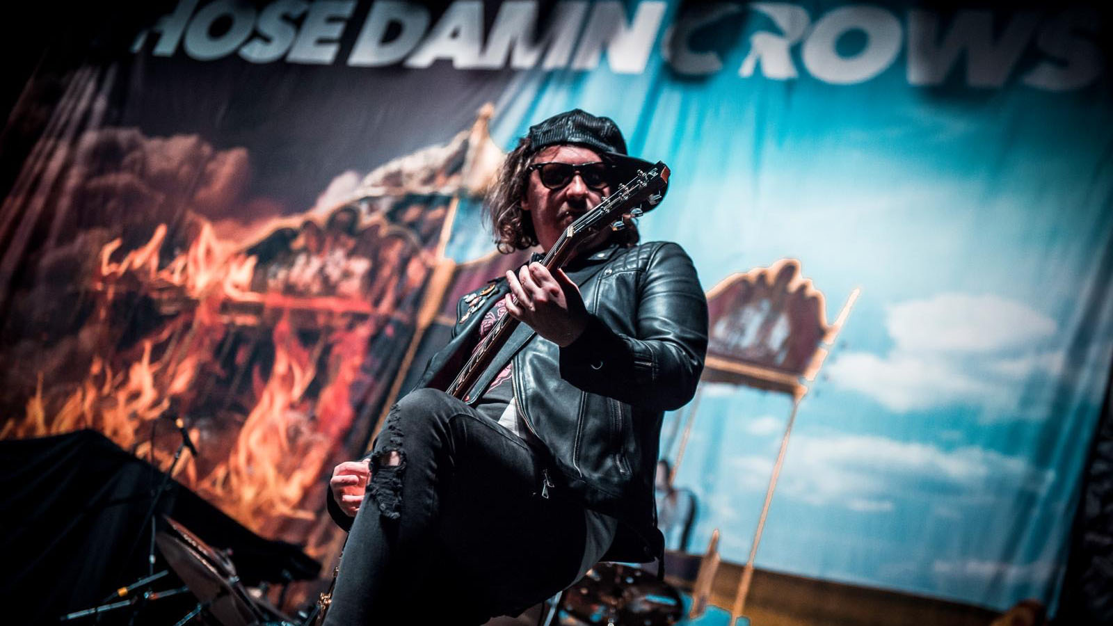 Ian "Shiner" Thomas of Those Damn Crows onstage playing to a festival crowd with his Gibson Les Paul. He wears a baseball cap and sunglasses.