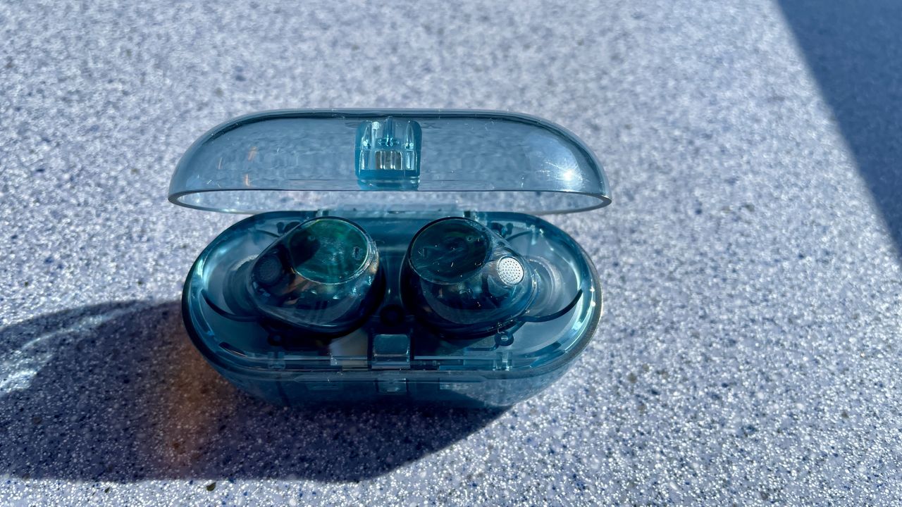 Sony WF-C710N earbuds in 'blue glass' on a grey table, with a woman's hand holding one of the earpieces