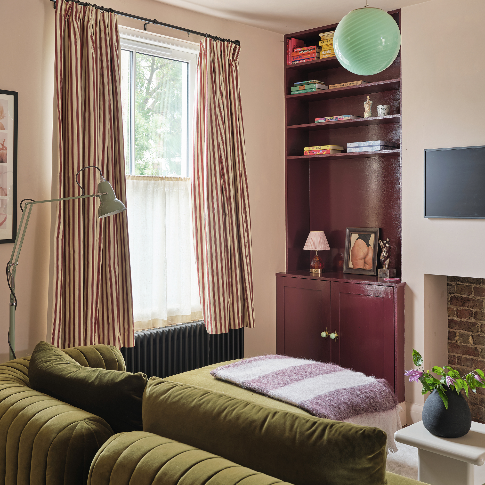 a small living room with a green velvet sofa and dark burgundy fitted alcove shelving and cabinetry and striped curtains