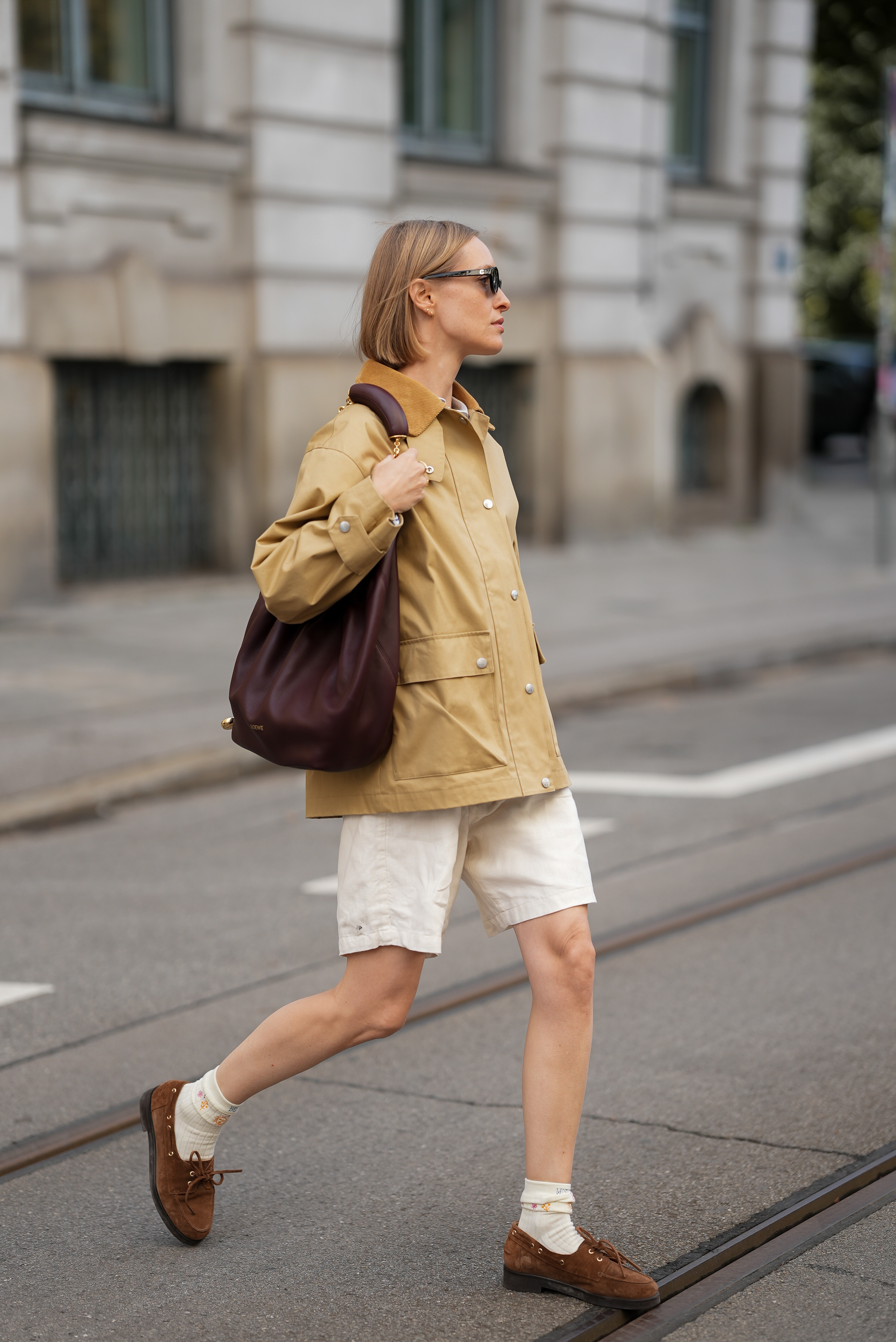 Person in driving loafers, slouchy leather bag, barn coat, and white shorts.